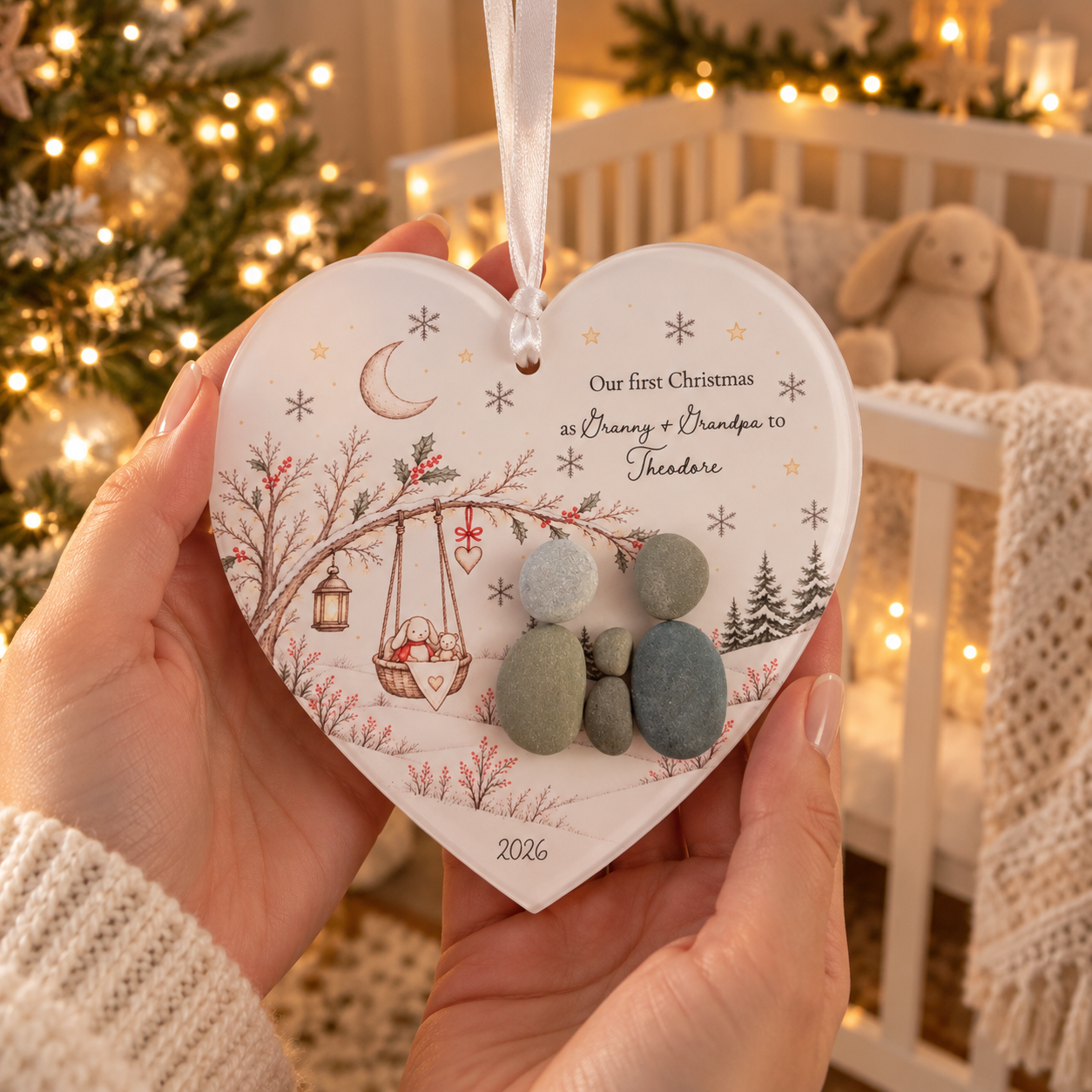 Hands holding the Our First Christmas as Granny + Grandpa to Theodore pebble decoration in a nursery