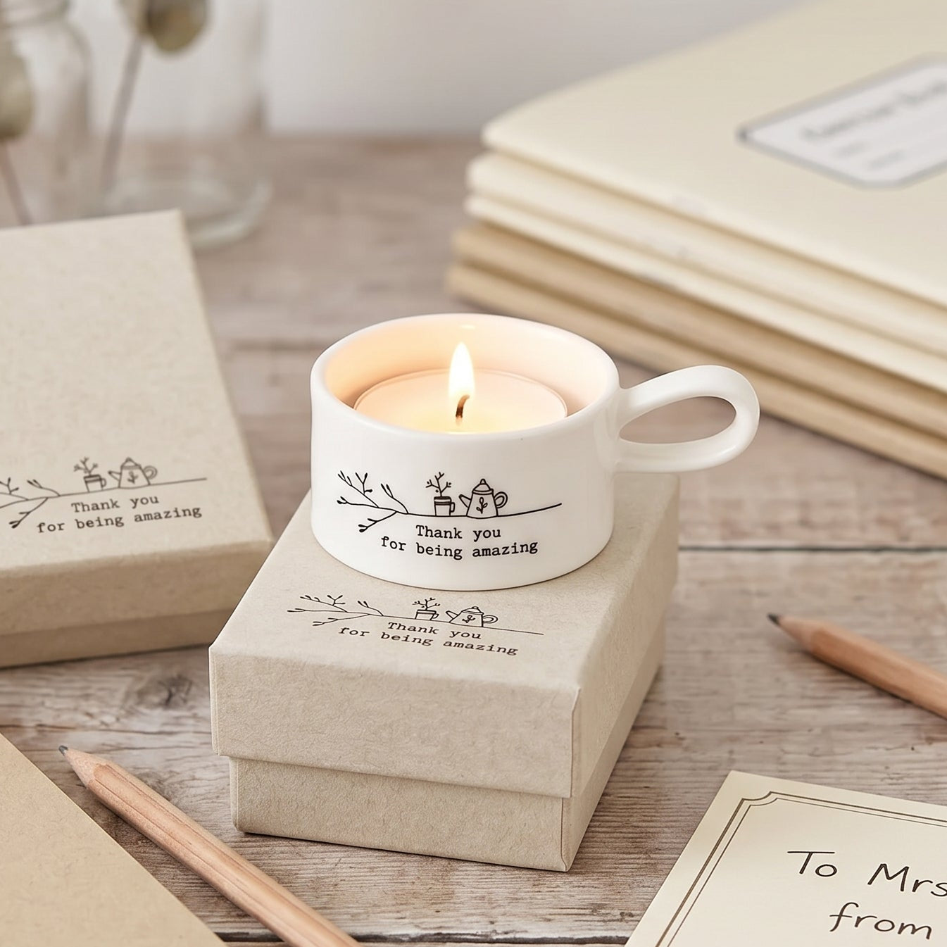 Candle in a mug with personalized message on a wooden surface with notebooks and pencils.