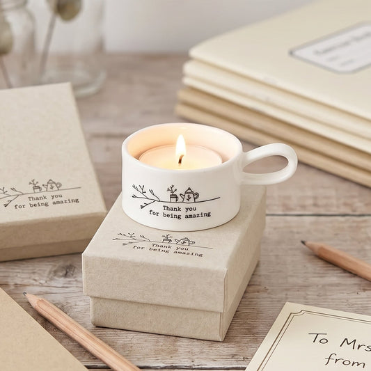 Candle in a mug with personalized message on a wooden surface with notebooks and pencils.
