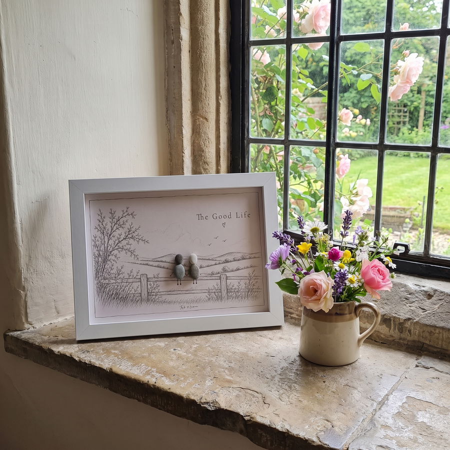 ‘The Good Life’ pebble picture on a stone windowsill beside a jug of garden flowers