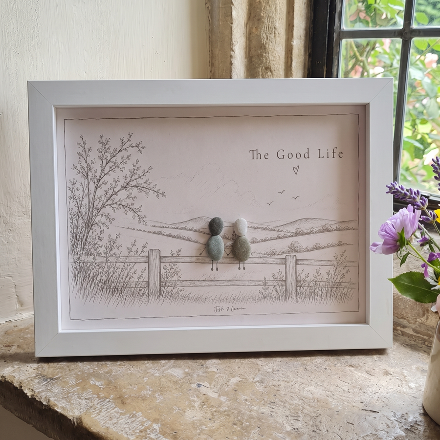 ‘The Good Life’ personalised pebble picture in a white frame on a cottage windowsill, two pebble people on a fence