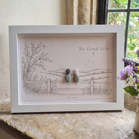 ‘The Good Life’ personalised pebble picture in a white frame on a cottage windowsill, two pebble people on a fence