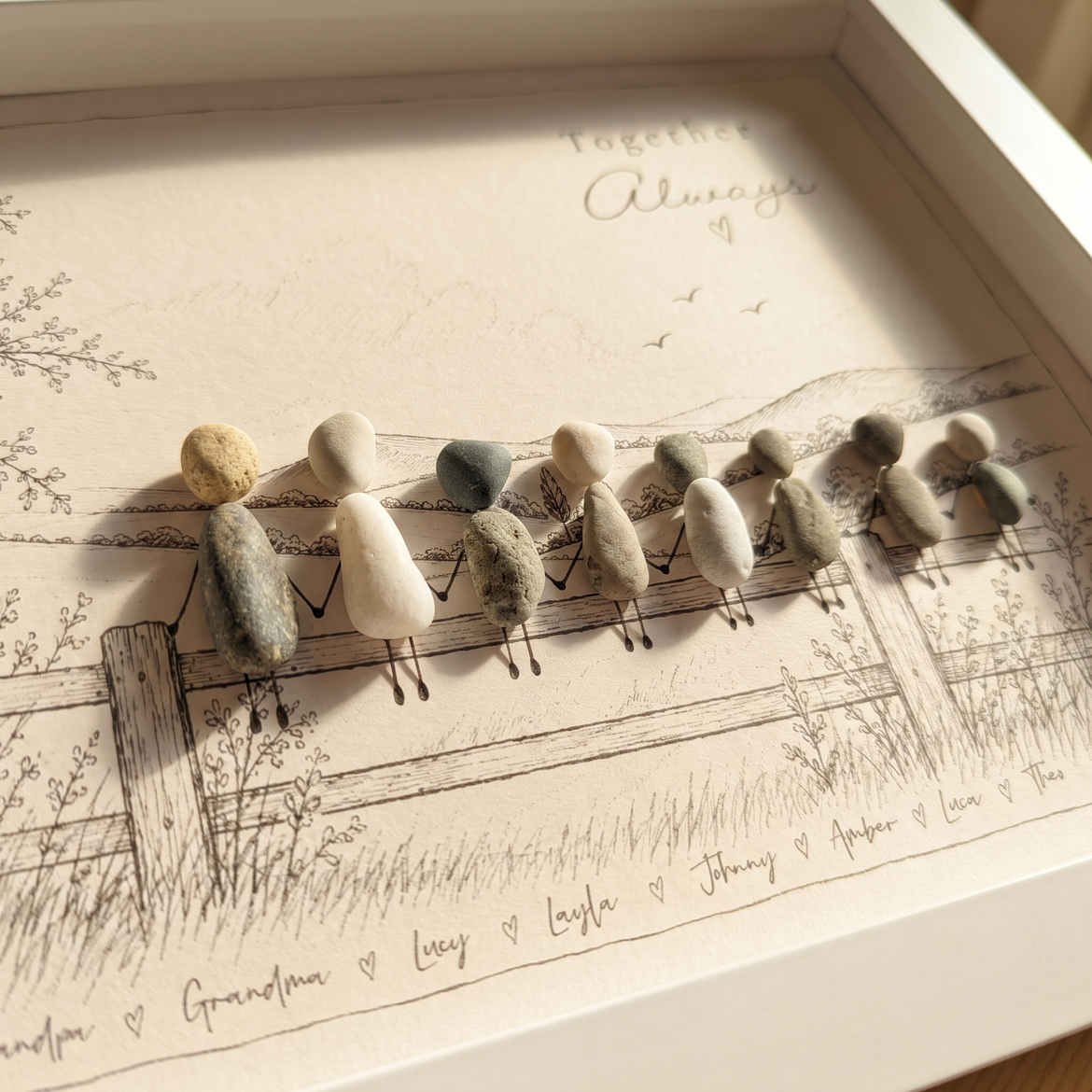Close-up of eight pebble people holding hands on a sketched fence with the family names written underneath