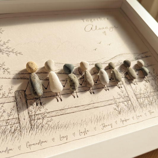 Close-up of eight pebble people holding hands on a sketched fence with the family names written underneath